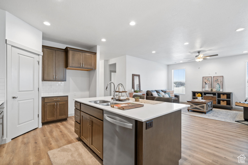 Kitchen featuring ceiling fan, light wood-type flooring, a center island with sink, tasteful backsplash, and dishwasher