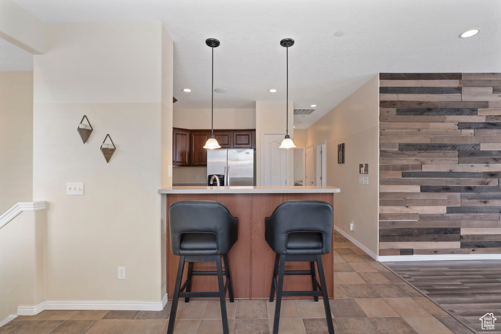 Kitchen featuring decorative light fixtures, a breakfast bar, stainless steel fridge with ice dispenser, dark brown cabinetry, and dark hardwood / wood-style flooring
