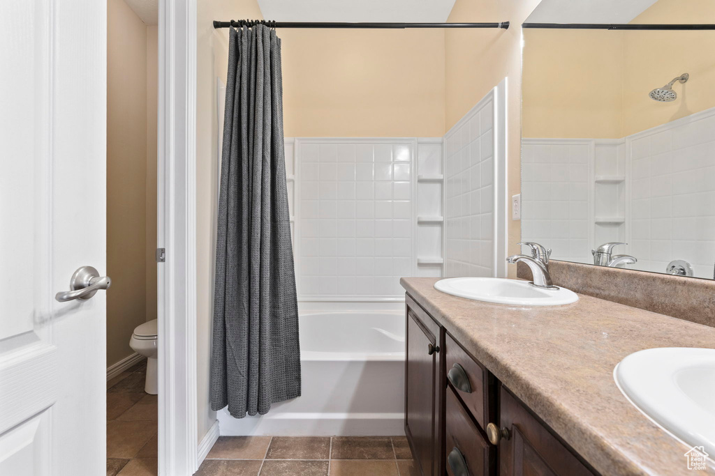 Full bathroom featuring tile flooring, toilet, dual bowl vanity, and shower / bathtub combination with curtain