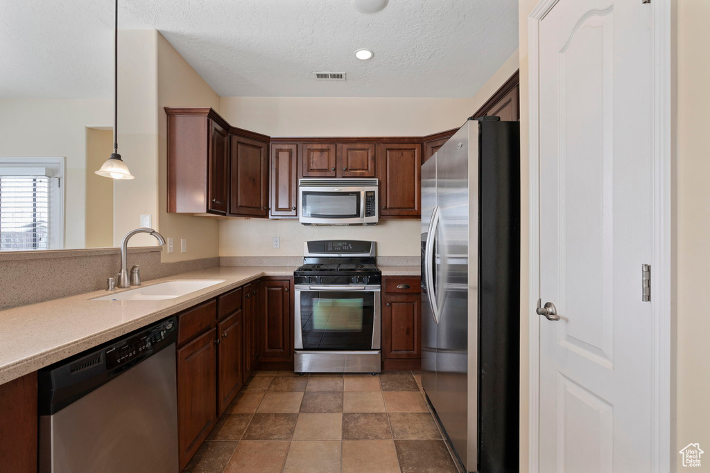 Kitchen with stainless steel appliances, hanging light fixtures, dark tile floors, dark brown cabinetry, and sink