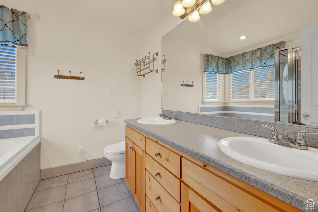 Bathroom with toilet, large vanity, tile flooring, dual sinks, and tiled tub