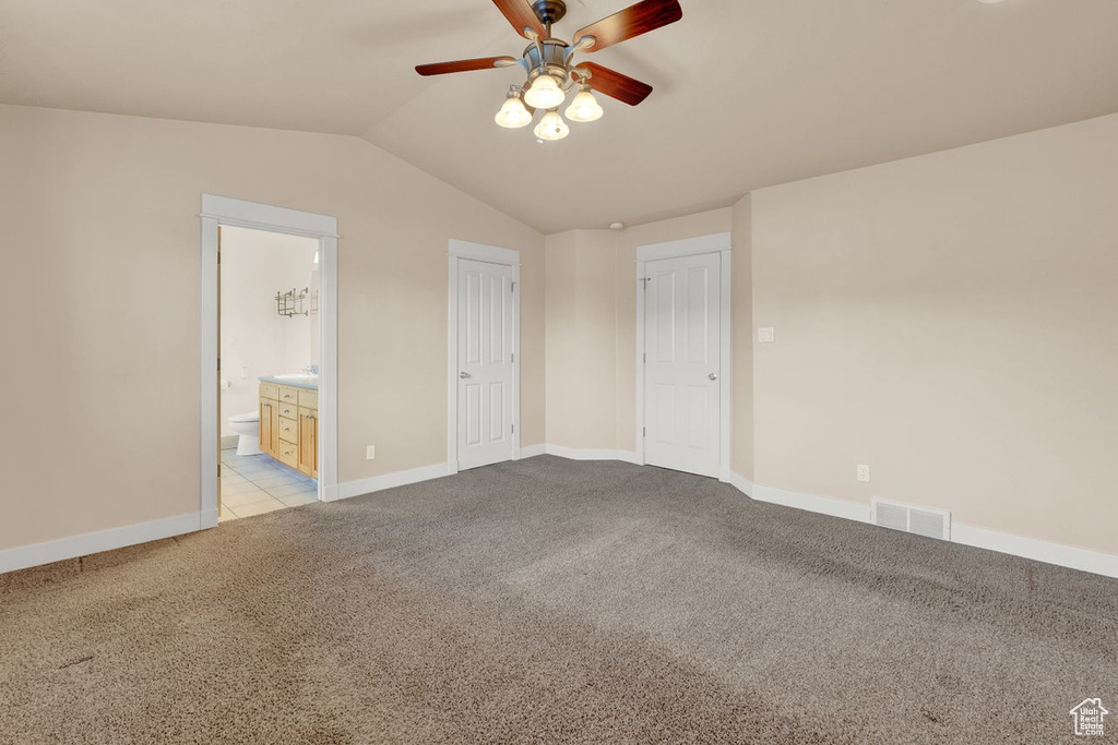 Interior space with light carpet, vaulted ceiling, ceiling fan, and ensuite bathroom