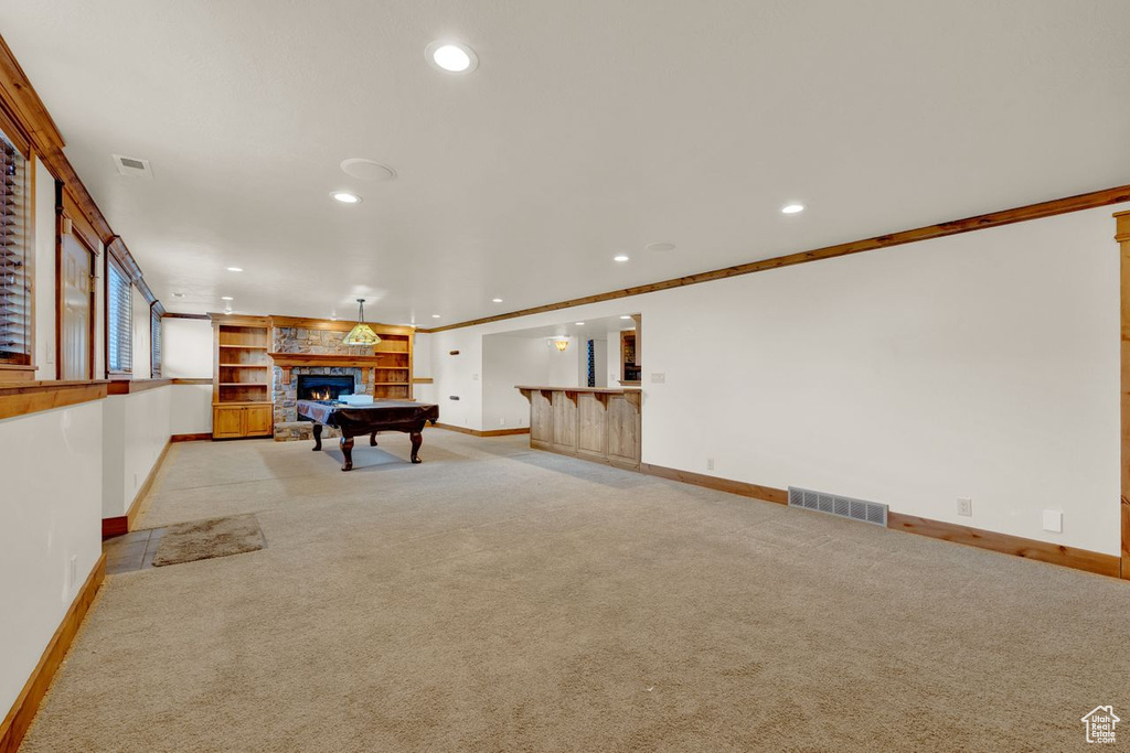 Interior space featuring light carpet, billiards, a stone fireplace, and ornamental molding