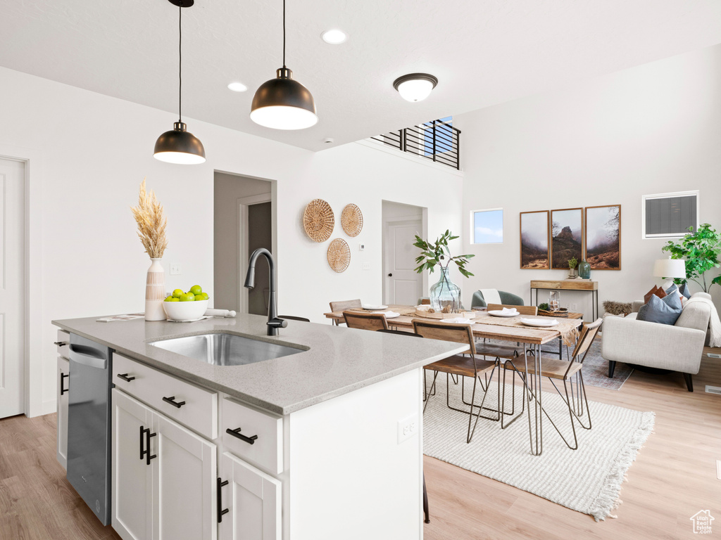 Kitchen featuring pendant lighting, white cabinetry, a kitchen island with sink, light wood-type flooring, and sink