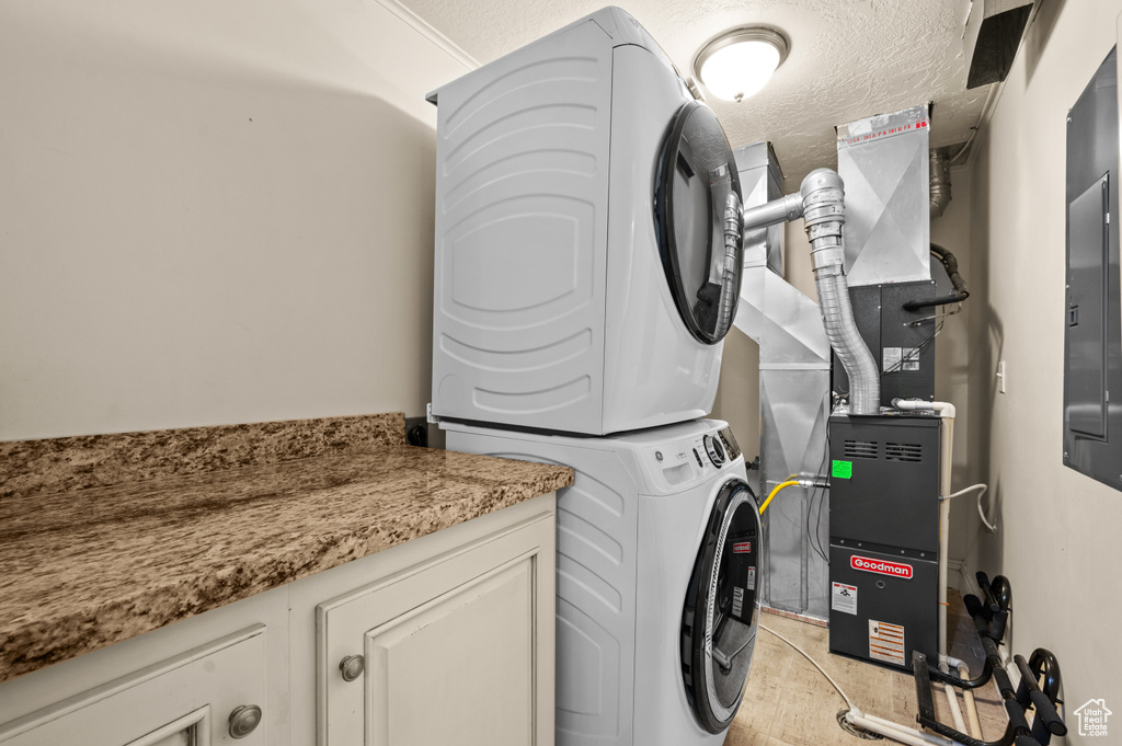 Clothes washing area with stacked washer / drying machine, cabinets, and a textured ceiling