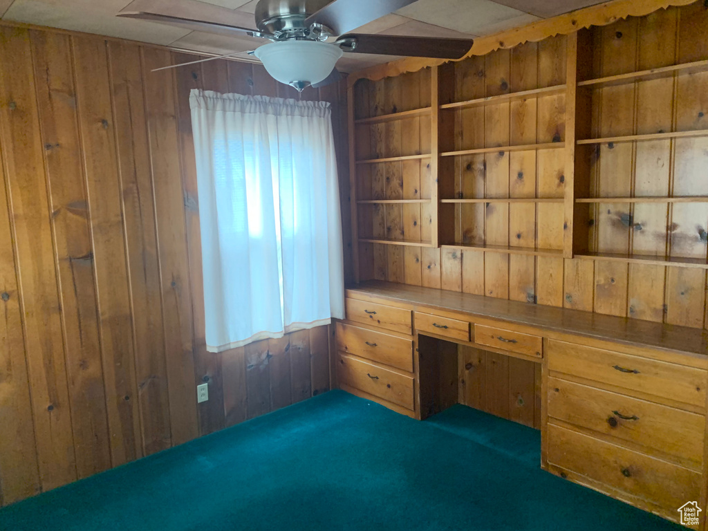 Carpeted spare room with wood walls, ceiling fan, and built in desk