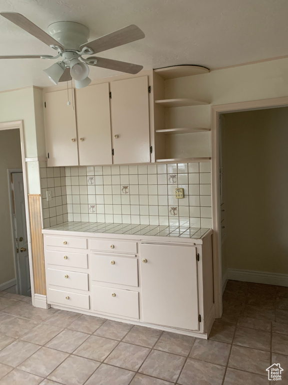 Kitchen with light tile floors, ceiling fan, white cabinetry, backsplash, and tile countertops
