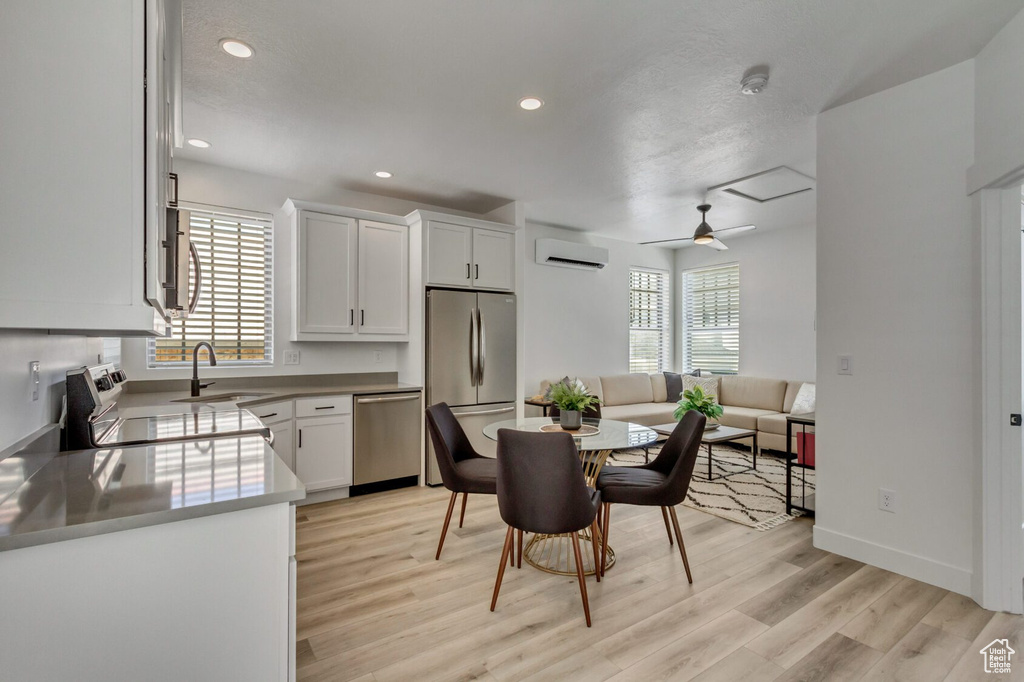 Kitchen with ceiling fan, a wall mounted air conditioner, white cabinets, appliances with stainless steel finishes, and light hardwood / wood-style floors
