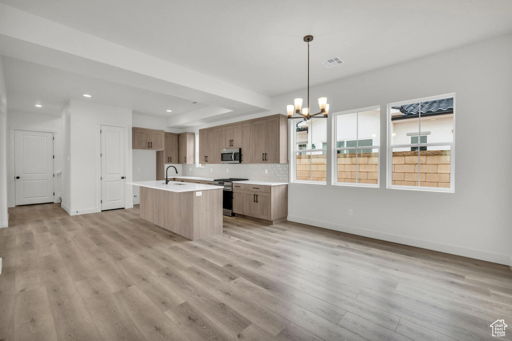 Kitchen featuring a chandelier, stainless steel appliances, a kitchen island with sink, and light wood-type flooring