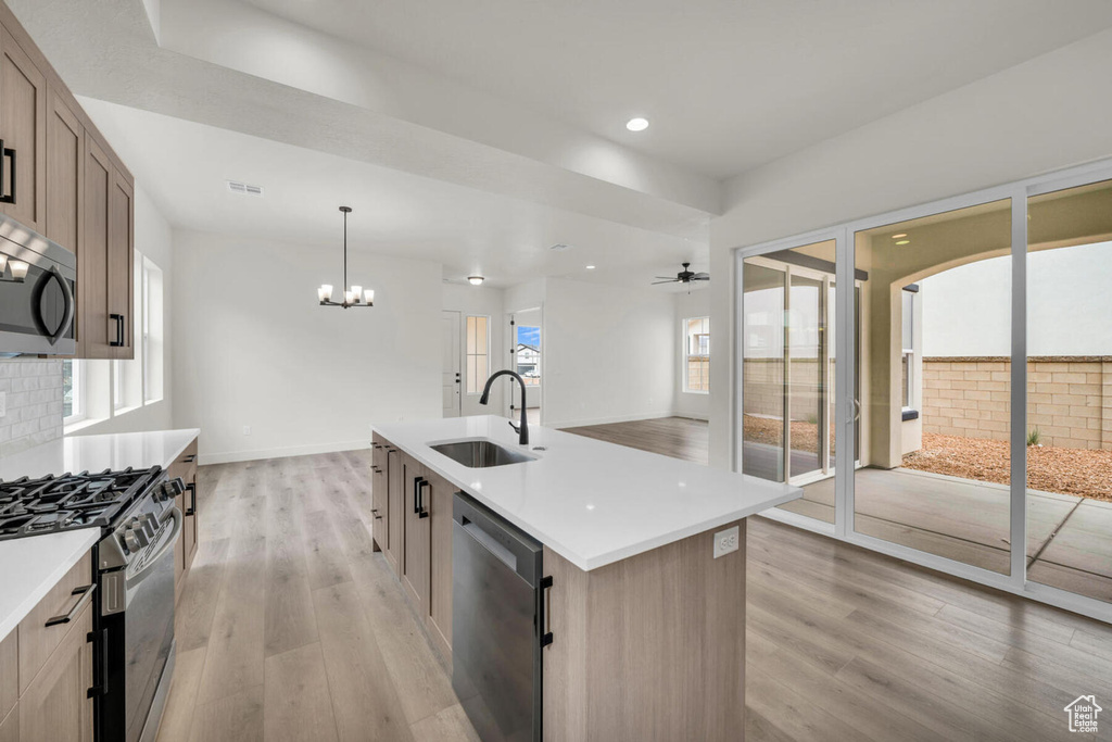 Kitchen with stainless steel appliances, decorative light fixtures, a center island with sink, light wood-type flooring, and sink