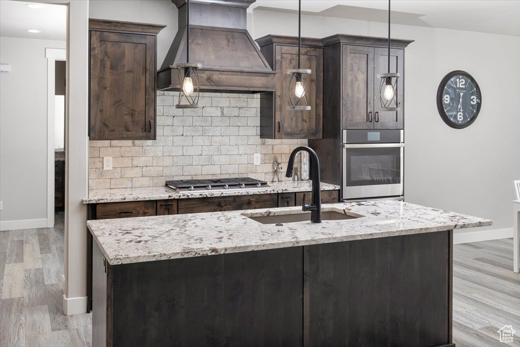 Kitchen featuring decorative light fixtures, custom range hood, light hardwood / wood-style floors, and stainless steel appliances