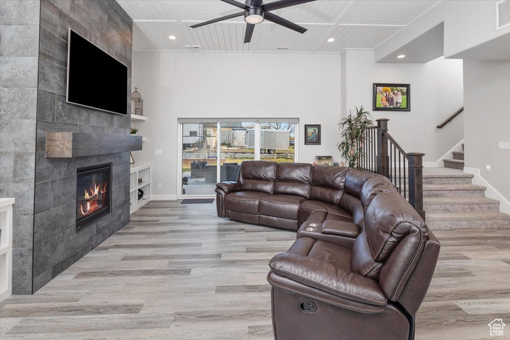 Living room featuring light hardwood / wood-style floors, a fireplace, wooden ceiling, ceiling fan, and tile walls
