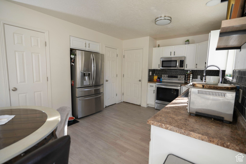 Kitchen with white cabinets, light hardwood / wood-style floors, tasteful backsplash, and stainless steel appliances