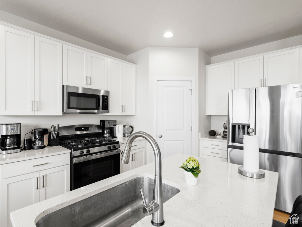 Kitchen with white cabinetry, sink, appliances with stainless steel finishes, and light stone counters