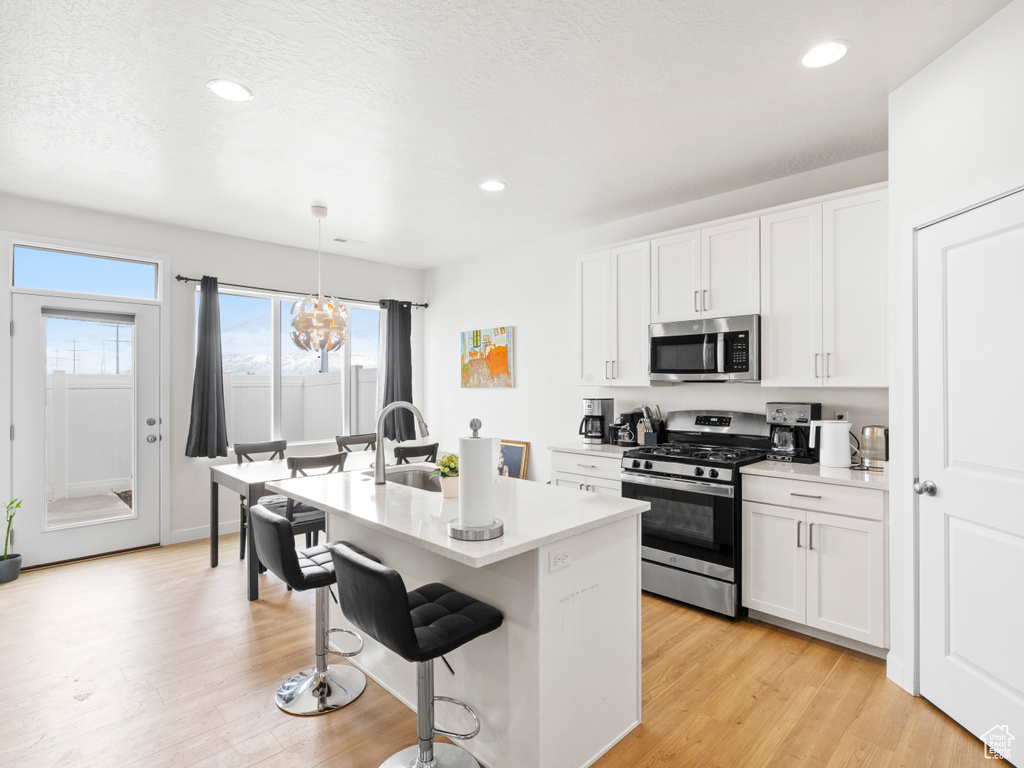 Kitchen featuring stainless steel appliances, a notable chandelier, decorative light fixtures, white cabinets, and light wood-type flooring