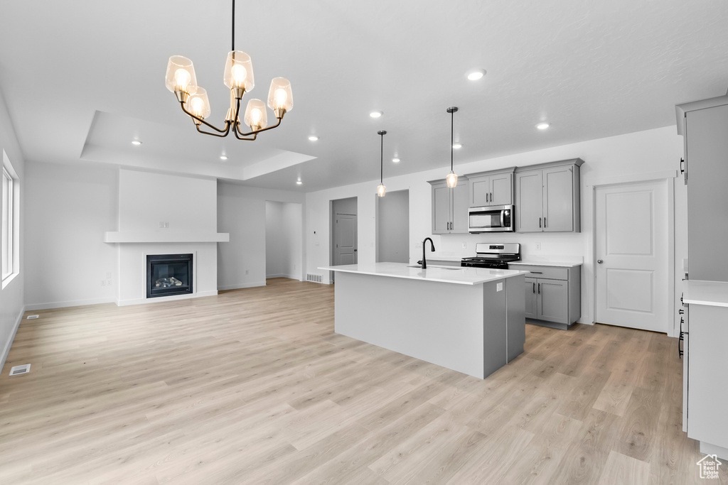 Kitchen featuring pendant lighting, an inviting chandelier, stainless steel appliances, light wood-type flooring, and a tray ceiling