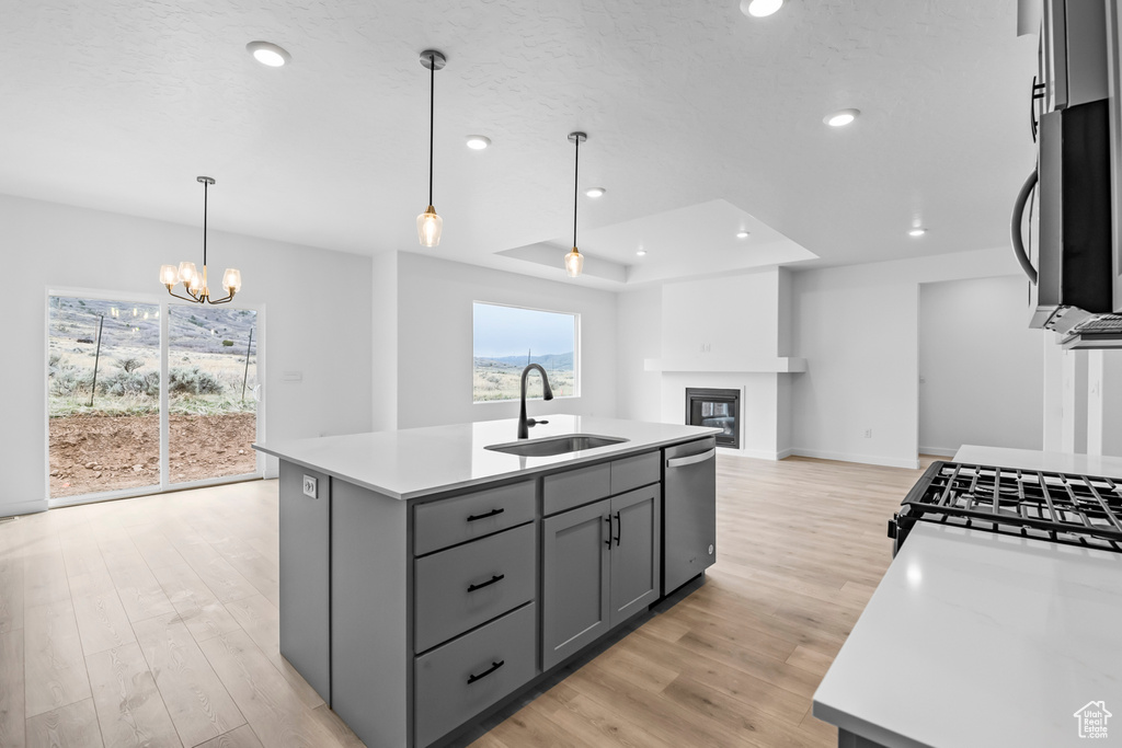 Kitchen with a kitchen island with sink, sink, light hardwood / wood-style floors, stainless steel appliances, and a chandelier