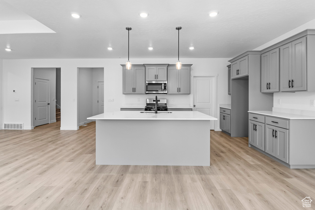 Kitchen with decorative light fixtures, appliances with stainless steel finishes, gray cabinets, and light hardwood / wood-style flooring