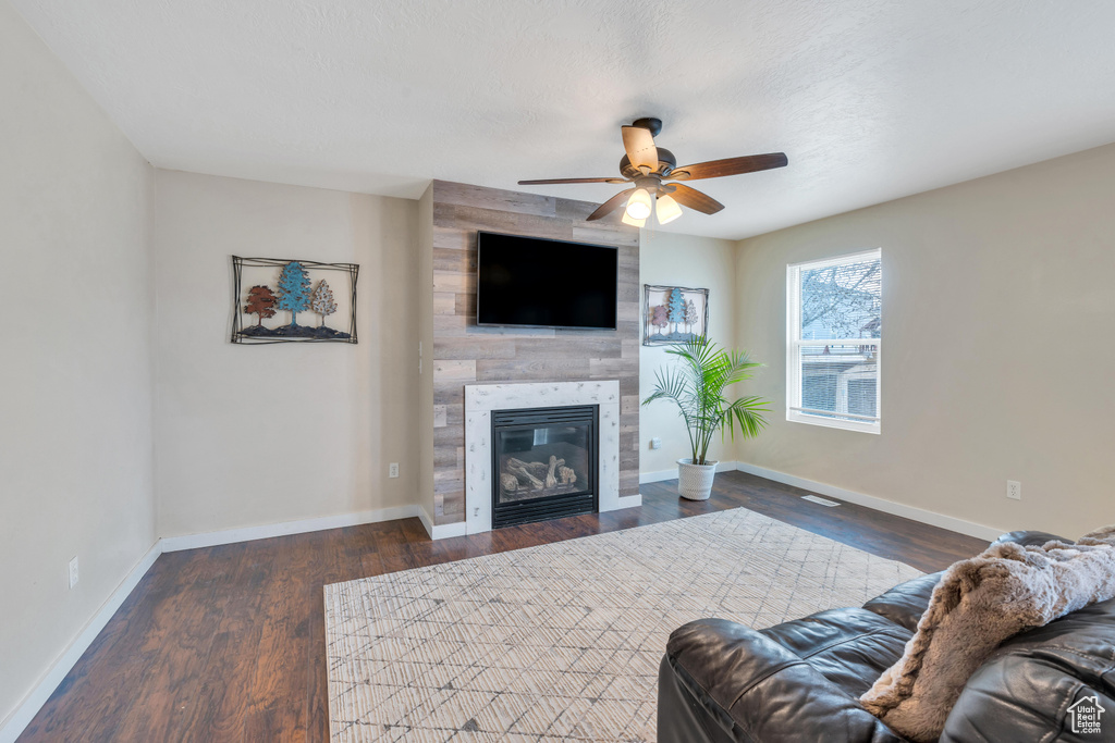 Living room featuring a tiled fireplace, dark hardwood / wood-style flooring, and ceiling fan