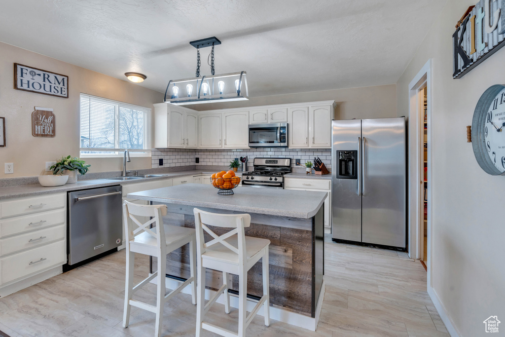 Kitchen with sink, hanging light fixtures, stainless steel appliances, white cabinetry, and a center island
