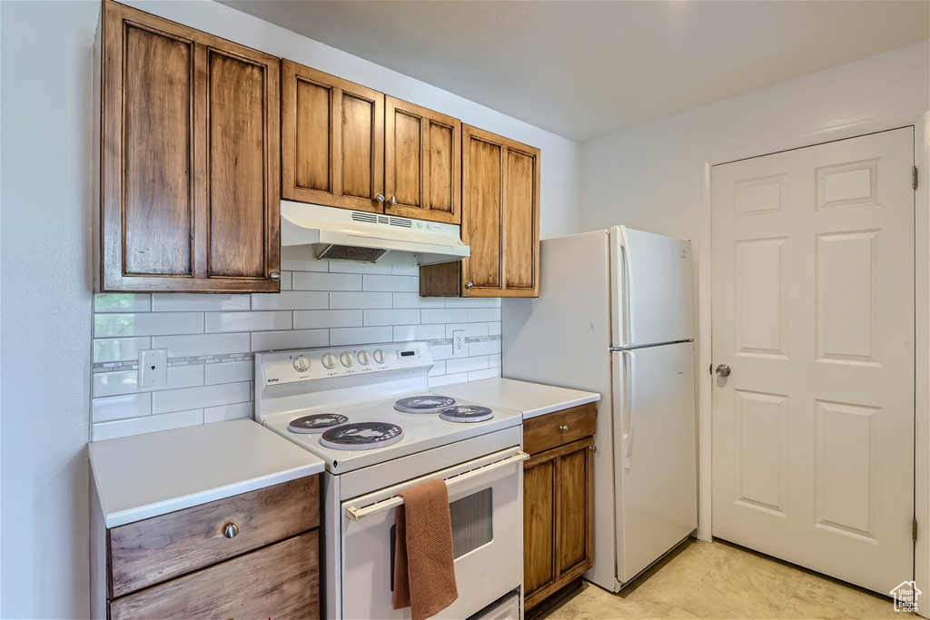 Kitchen with white appliances, tasteful backsplash, and light tile floors