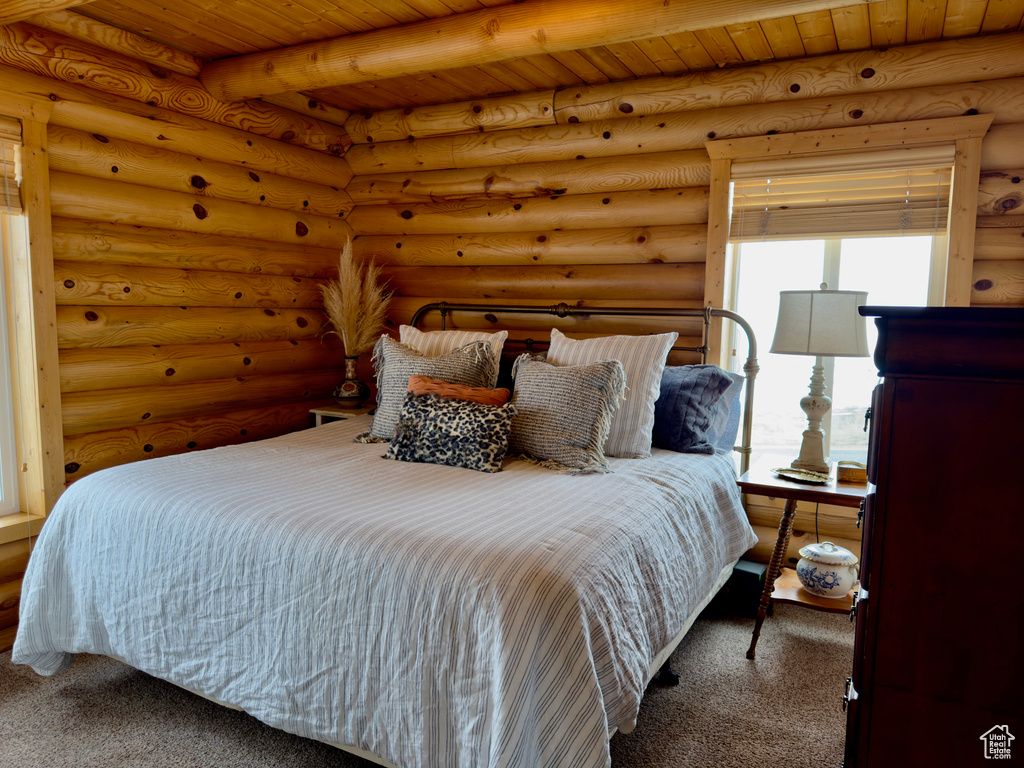 Carpeted bedroom with rustic walls, wooden ceiling, and beamed ceiling