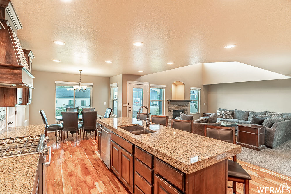 Kitchen with an island with sink, a chandelier, pendant lighting, a fireplace, and premium range hood