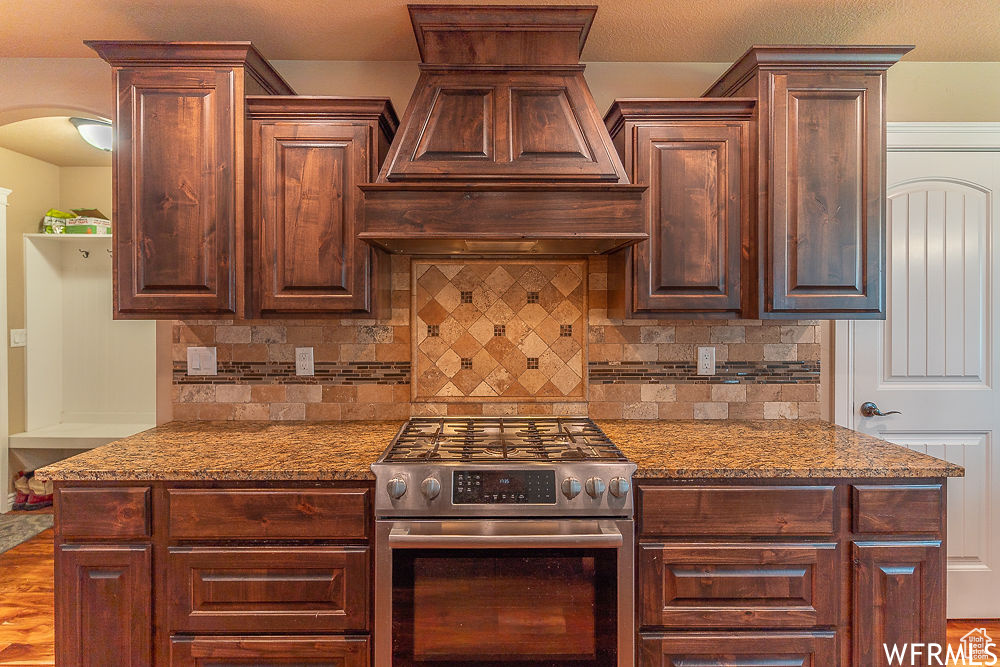 Kitchen featuring tasteful backsplash, stone countertops, stainless steel range with gas stovetop, and premium range hood