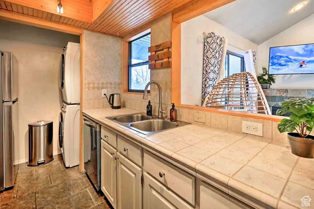Kitchen featuring wood ceiling, sink, stacked washer and dryer, tasteful backsplash, and tile countertops