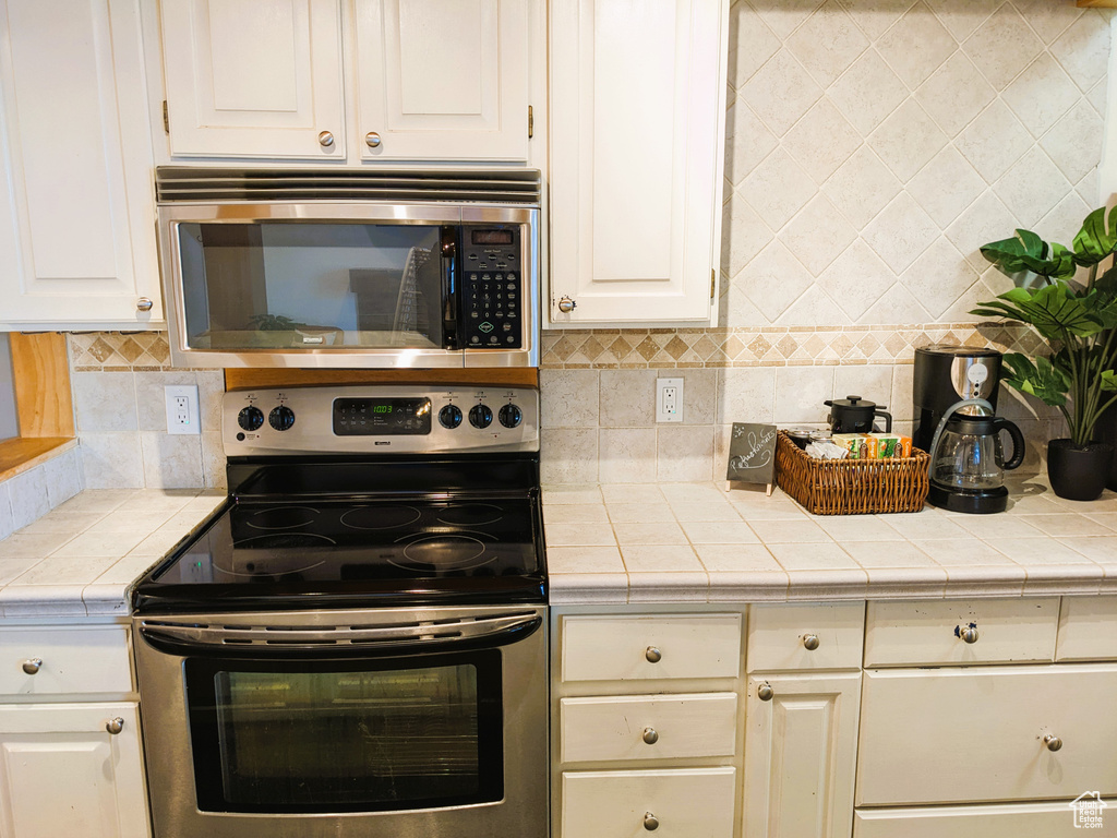 Kitchen with appliances with stainless steel finishes, tasteful backsplash, tile countertops, and white cabinetry