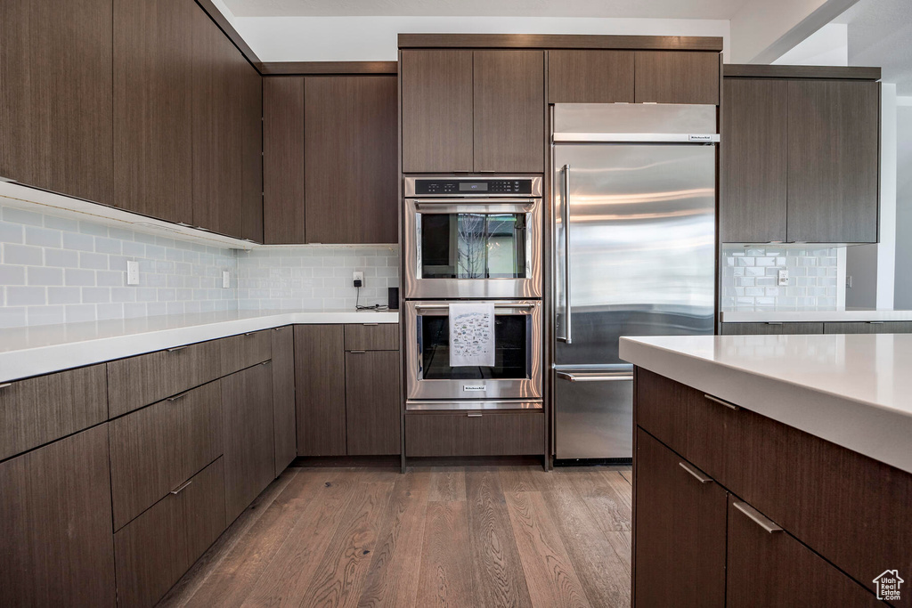 Kitchen with wood-type flooring, dark brown cabinetry, tasteful backsplash, and appliances with stainless steel finishes