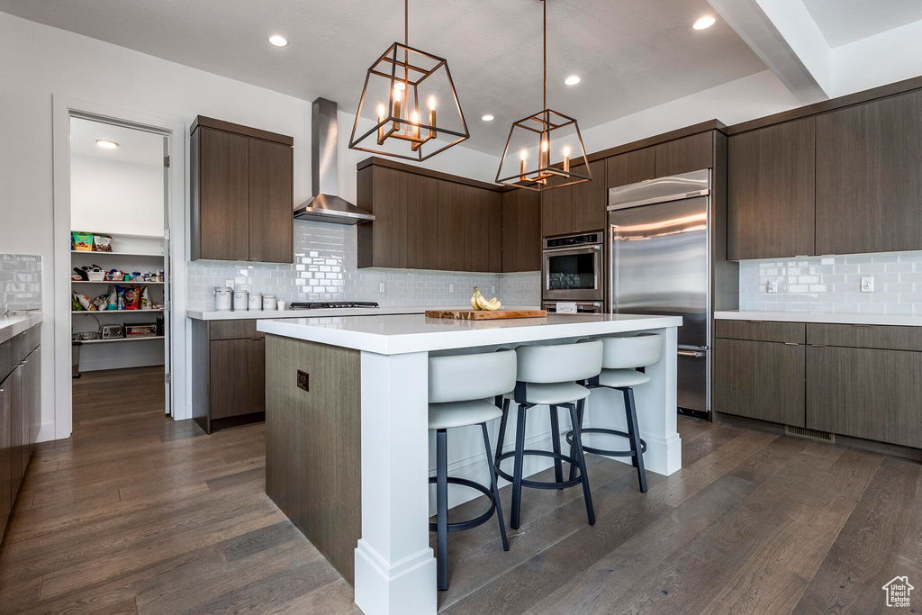 Kitchen with pendant lighting, a kitchen island, wall chimney range hood, tasteful backsplash, and dark hardwood / wood-style floors