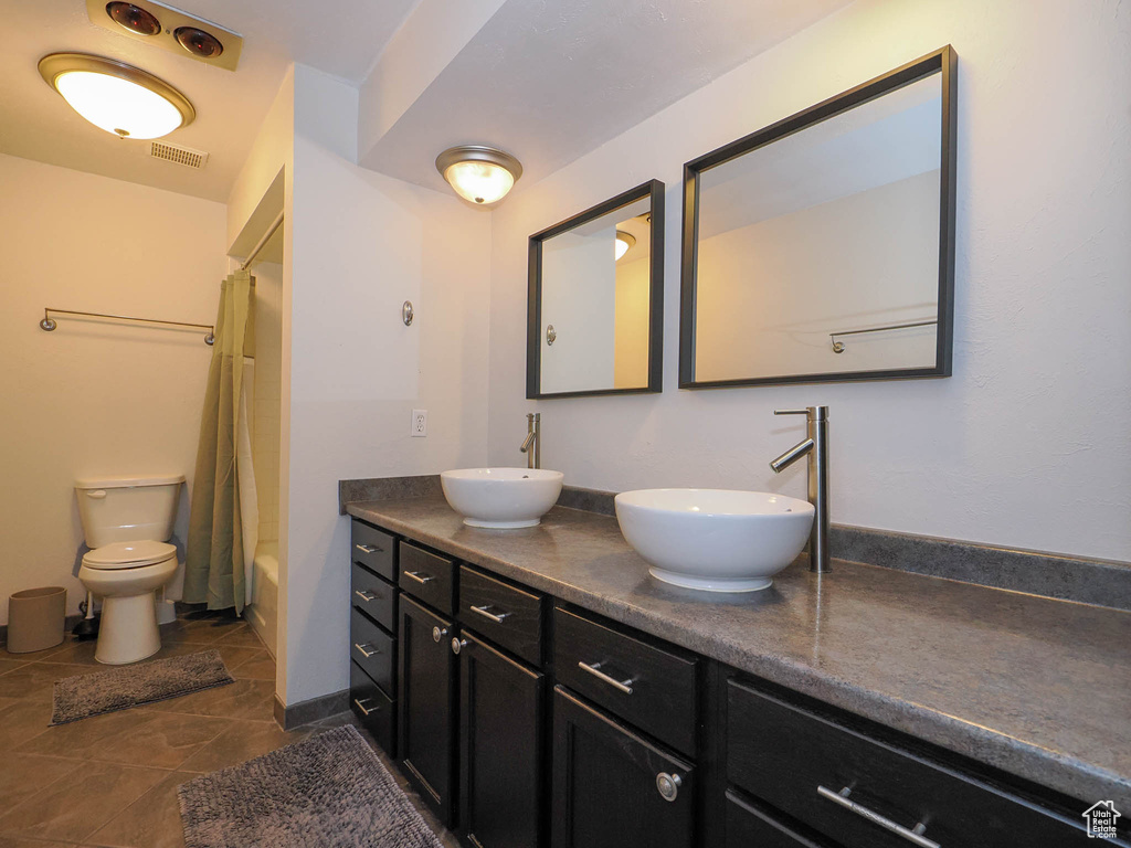 Full bathroom with dual vanity, tile flooring, toilet, and shower / bathtub combination with curtain