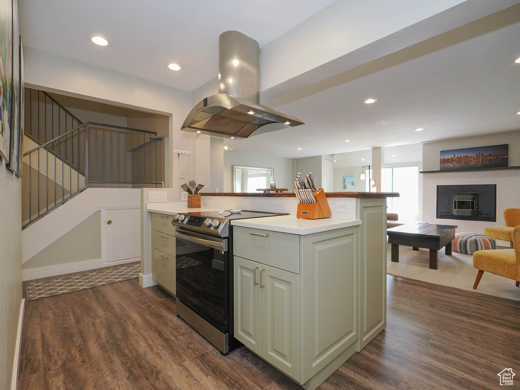 Kitchen with island range hood, green cabinets, stainless steel range with electric stovetop, dark wood-type flooring, and a tiled fireplace