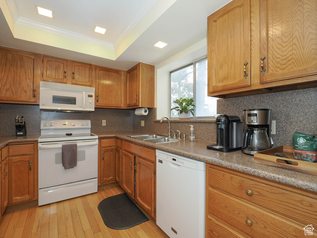 Kitchen with tasteful backsplash, white appliances, a tray ceiling, light wood-type flooring, and sink