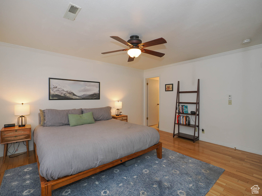 Bedroom with light hardwood / wood-style floors, ornamental molding, and ceiling fan