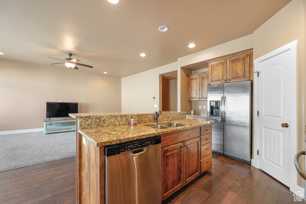 Kitchen with ceiling fan, appliances with stainless steel finishes, sink, an island with sink, and dark colored carpet