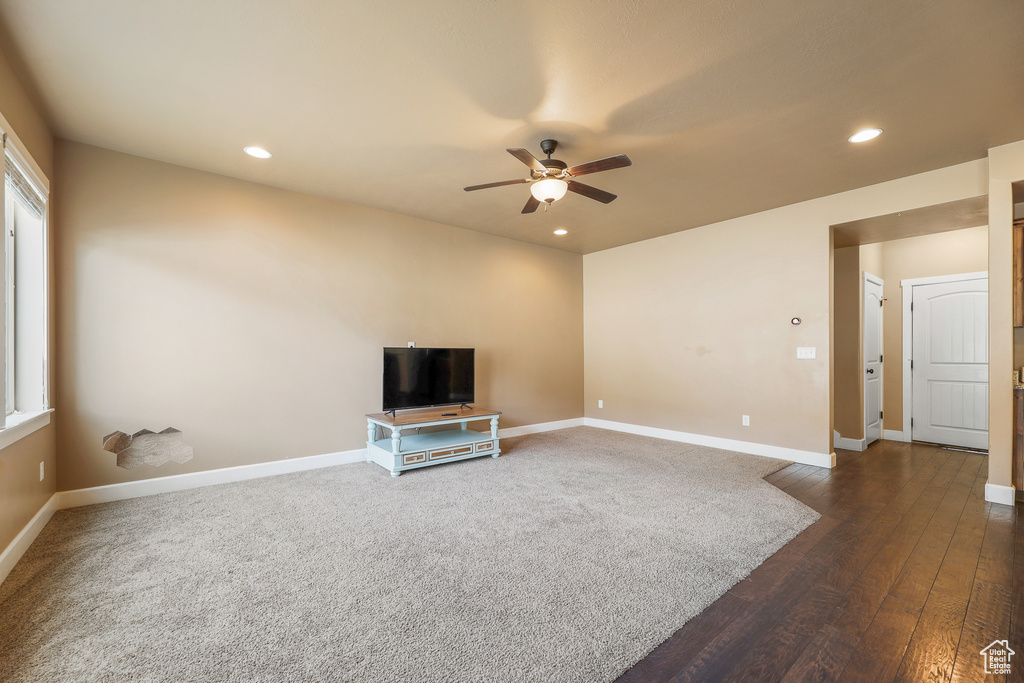 Unfurnished living room featuring plenty of natural light, ceiling fan, and dark colored carpet