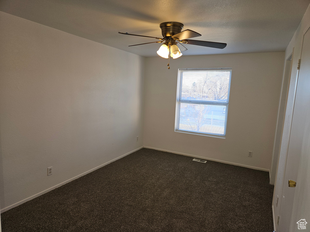 Spare room featuring ceiling fan and dark colored carpet