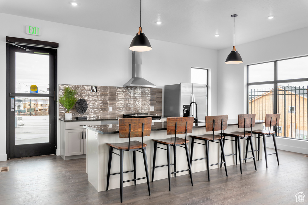 Kitchen featuring tasteful backsplash, a breakfast bar area, a wealth of natural light, and wall chimney range hood