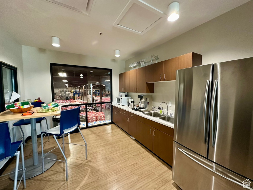 Kitchen featuring sink, dark brown cabinets, stainless steel refrigerator, and light wood-type flooring