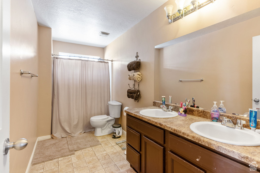 Bathroom featuring tile floors, toilet, dual vanity, and a textured ceiling