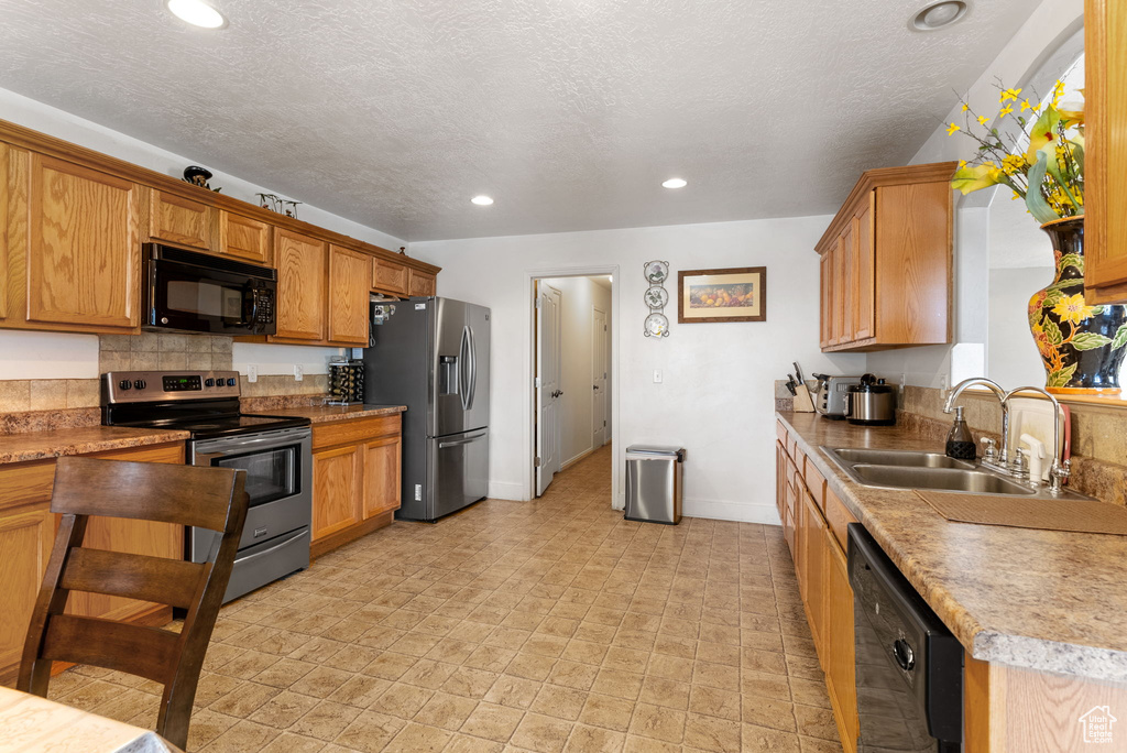 Kitchen featuring sink, light tile flooring, black appliances, tasteful backsplash, and a textured ceiling