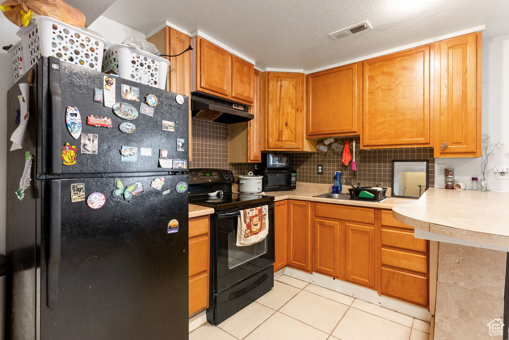 Kitchen with tasteful backsplash, a textured ceiling, light tile floors, and black appliances