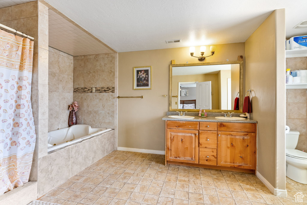 Bathroom featuring dual vanity, tile floors, a textured ceiling, toilet, and tiled tub