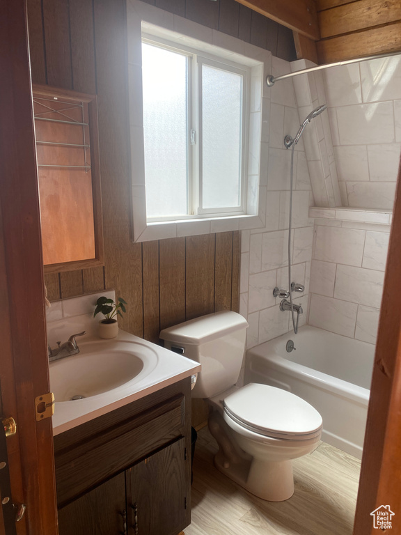 Full bathroom featuring toilet, tiled shower / bath combo, vanity, wooden walls, and wood-type flooring