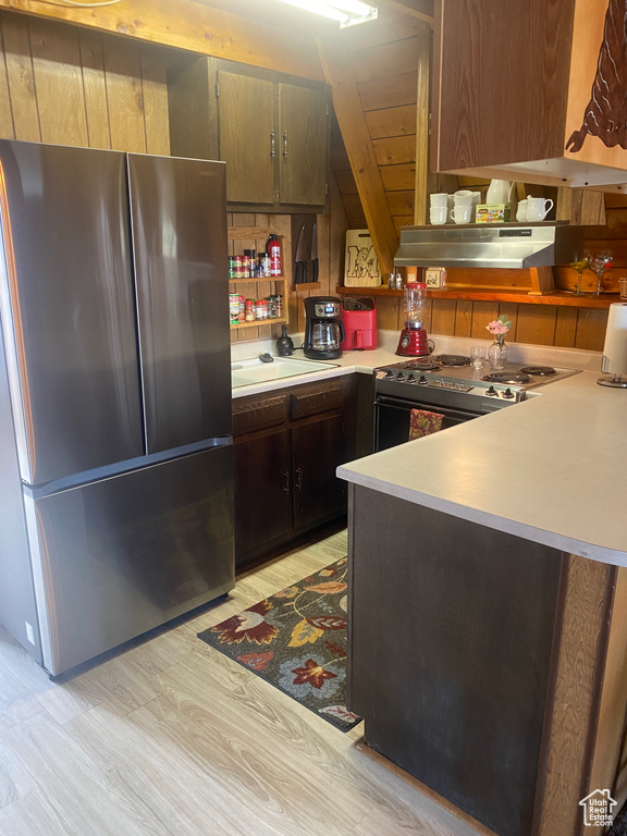 Kitchen with light hardwood / wood-style floors, dark brown cabinets, wall chimney exhaust hood, white electric stove, and stainless steel refrigerator