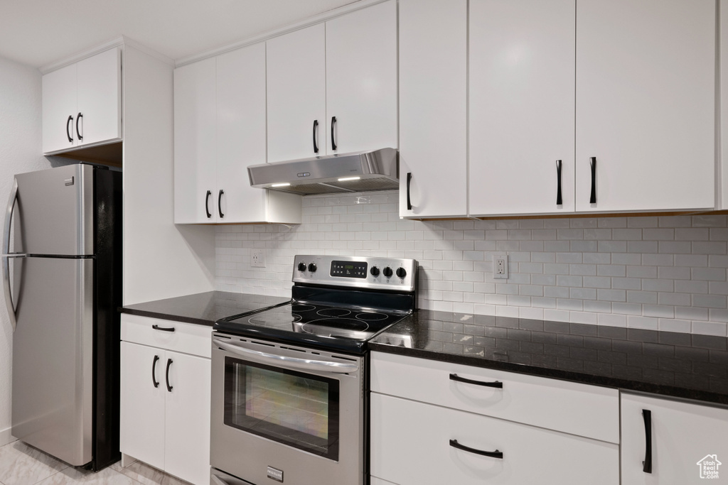 Kitchen featuring stainless steel appliances, light tile floors, white cabinets, dark stone countertops, and tasteful backsplash