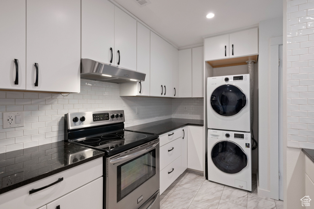 Kitchen with electric stove, light tile floors, white cabinets, tasteful backsplash, and stacked washing maching and dryer