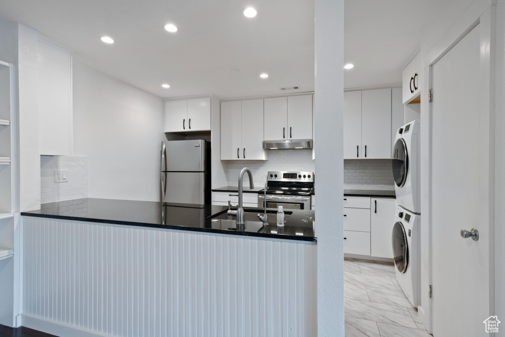 Kitchen featuring light tile floors, stacked washer and dryer, tasteful backsplash, appliances with stainless steel finishes, and white cabinets